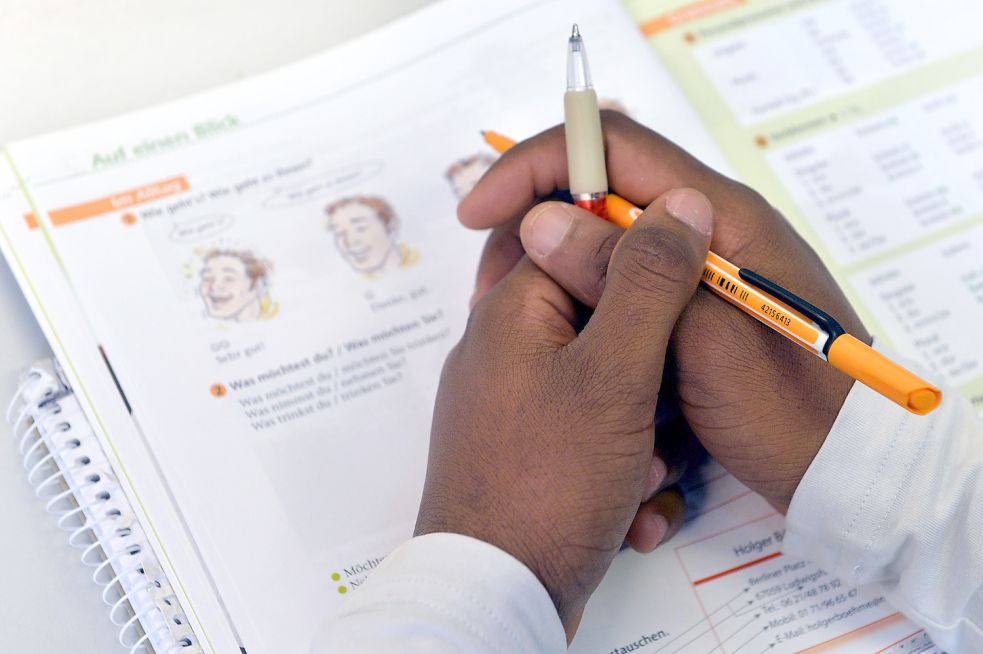 Ein Lehrbuch liegt in einem Deutschkurs für Flüchtlinge vor einem jungen Mann auf der Schulbank. Foto: Schmidt/dpa