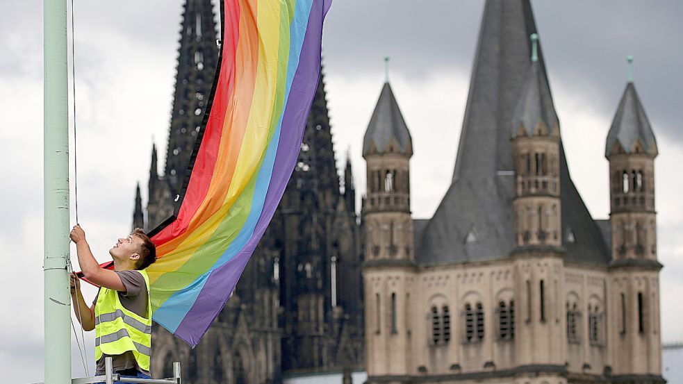 Eine Regenbogenfahne vor der Kulisse des Kölner Doms und der Kirche Groß St. Martin (rechts). Foto: Berg/DPA