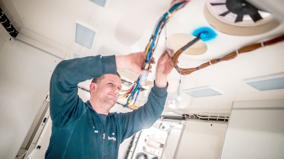 Mitarbeiter Gregor Adams arbeitet an einem Kabelbaum, der im Himmel eines Transportwagens befestigt wird. Foto: Cordsen