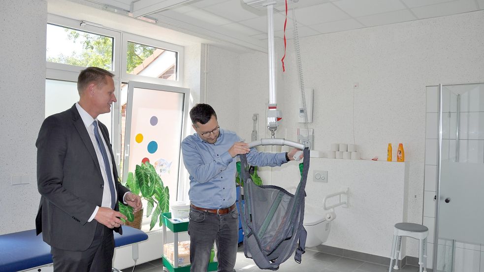 Schulleiter Armin Feldmann (rechts) erklärt Landrat Holger Heymann die Handhabung des Traversenlifts. In das Tuch werden die Schüler gesetzt und können so beispielsweise sitzend in die Dusche gebracht werden. Foto: Ullrich