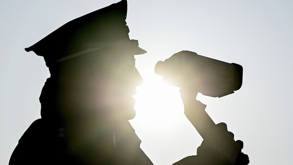 Mit einer Laserpistole steht ein Polizist vor einer Schule und misst die Geschwindigkeit der Fahrzeuge. Foto: Patrick Pleul/dpa