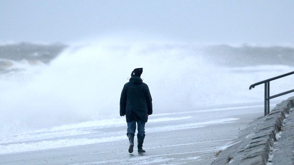 Eine Spaziergängerin läuft bei stürmischem Wetter am Strand von Norderney. Foto: Bartels/dpa