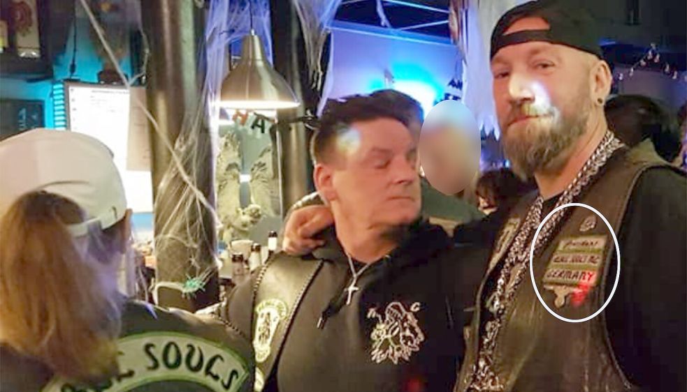 Noch ein Rocker des "Rebel Souls MC" (rechts) mit Reichsadler und Totenkopf. Die Schriftzüge auf der Kutte sind schwer lesbar – aber es könnte sich demnach um einen früheren "President" des Clubs handeln. Das Foto haben die Rocker am 27. Oktober 2019 auf ihrer Facebook-Seite veröffentlicht. Foto: Screenshot (Ausschnitt) vom 04.02.2024 / Quelle: Facebook-Seite des Rebel Souls MC Großefehn / Pixelung, Ausschnitt und Hervorhebung (weiße Ellipse): OZ