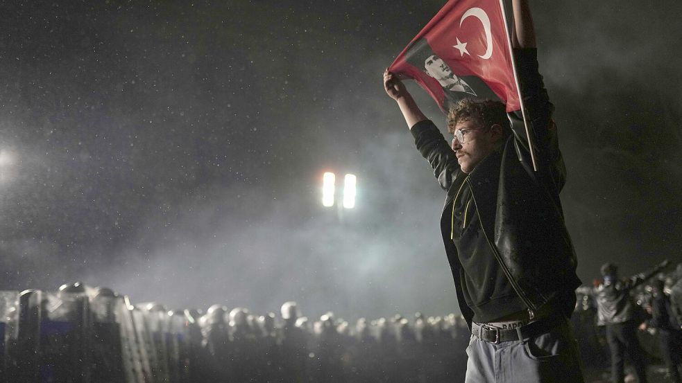 Ein Demonstrant hält in Istanbul eine türkische Flagge, während Bereitschaftspolizisten bei einer Demonstration nach der Verhaftung und Inhaftierung des Istanbuler Bürgermeisters Imamoglu Wache stehen. Foto: Seco/AP/DPA
