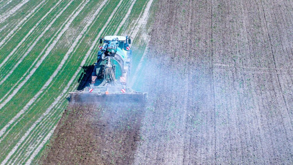 Ein Traktor zieht einen Düngehänger über ein trockenes Feld und wirbelt eine Staubwolke auf (Aufnahme mit Drohne). Foto: Büttner/dpa