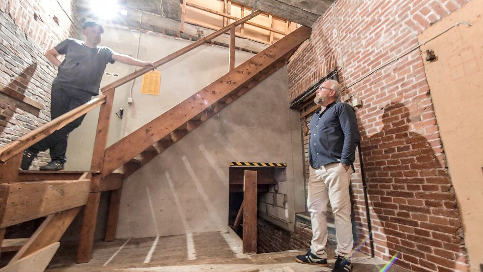 Henk (links) und Dirk Strobel stehen im Durchgang, der derzeit keiner mehr ist. Die Wand hinter der Treppe wurde irgendwann samt Zwischendecke neu eingezogen. Das soll wieder rückgängig gemacht werden. Foto: Klaus Ortgies