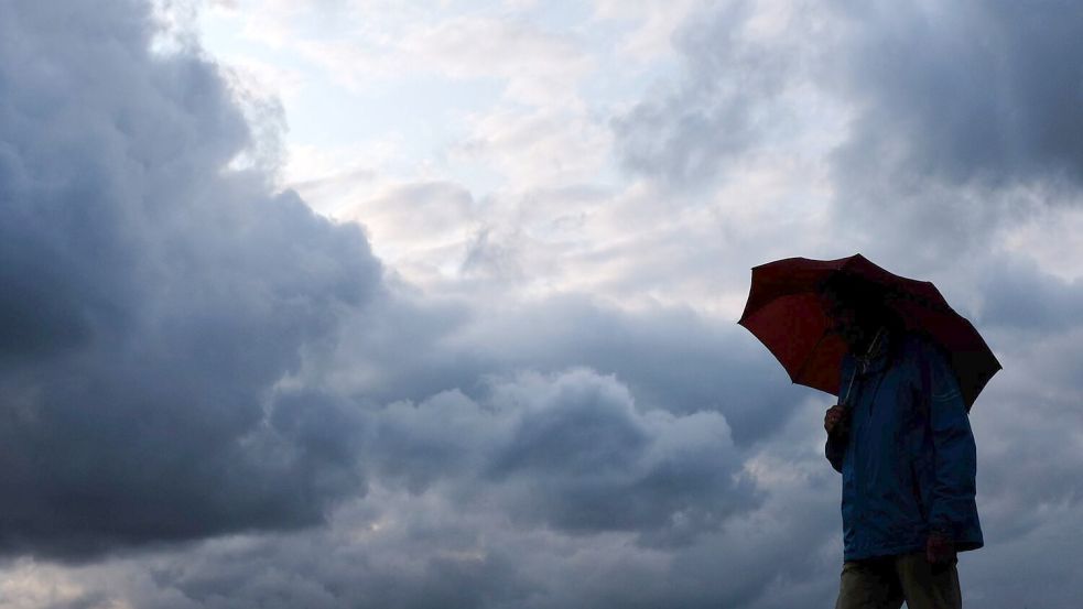 Ein Mann geht mit einem Regenschirm vor aufziehenden dunklen Wolken spazieren. Das Wetter an diesem Wochenende in Ostfriesland wird stürmisch mit viel Regen. Symbolfoto: Martin Gerten/dpa