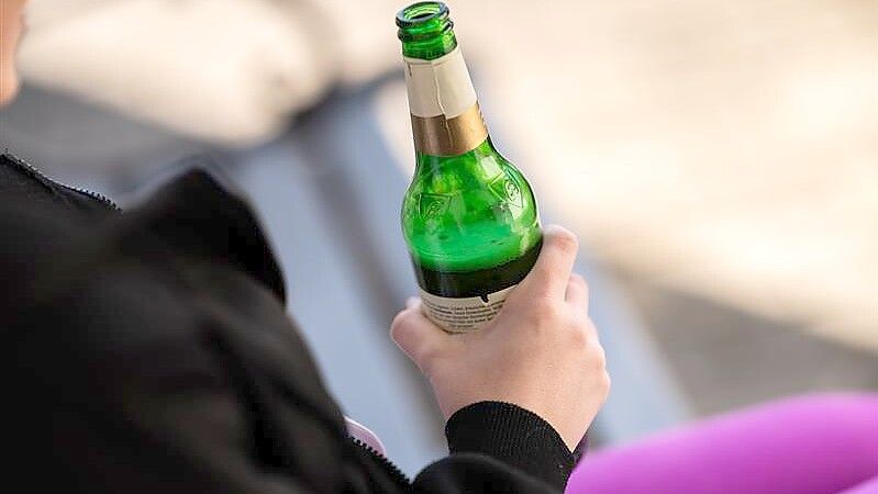 Eine Frau sitzt und hält eine Bierflasche in der Hand. Wenn eine Person stark berauscht ist und hilflos wird, vielleicht sogar von anderen bedrängt wird, sollte man nicht einfach wegschauen, sondern helfen, findet eine Emderin. Symbolfoto: Silas Stein/dpa