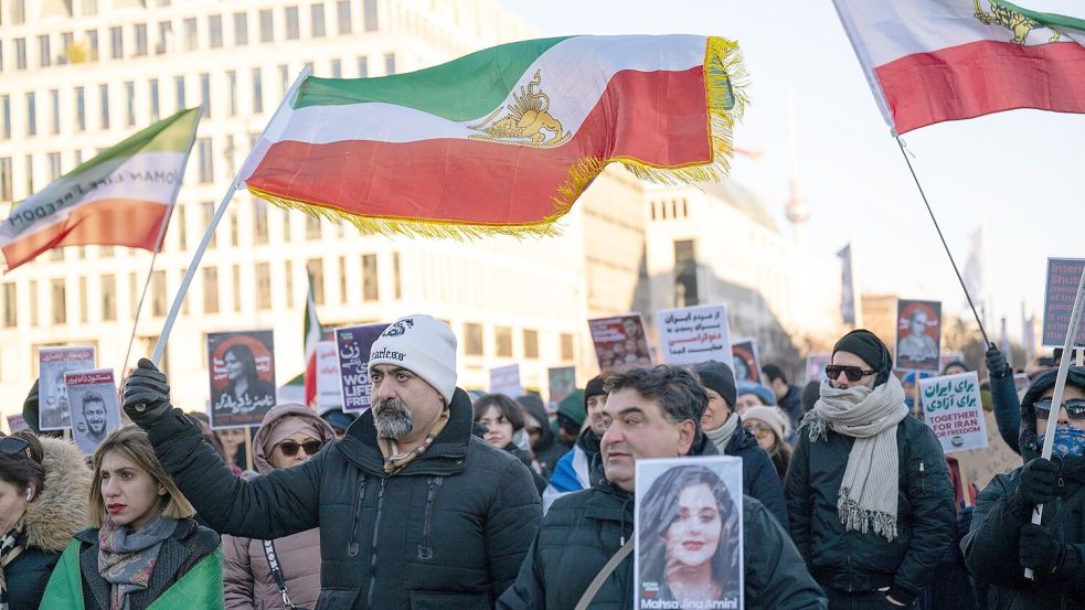Teilnehmer einer Demonstration halten während einer Kundgebung vor dem Brandenburger Tor zur Unterstützung der landesweiten Massendemonstrationen im Iran gegen die Regierung Plakate und Iran-Flaggen. Foto: Christophe Gateau/dpa