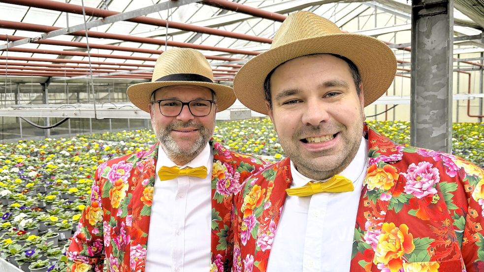Nils Hasselhorn (links) und Sven Ewen in einem ihrer Gewächshäuser in Wiesmoor: Mit Strohhut, gelber Fliege und Blumenanzug sind die beiden als „Blumenmänner“ auf Kunsthandwerkermärkten unterwegs. Foto: Nicole Böning
