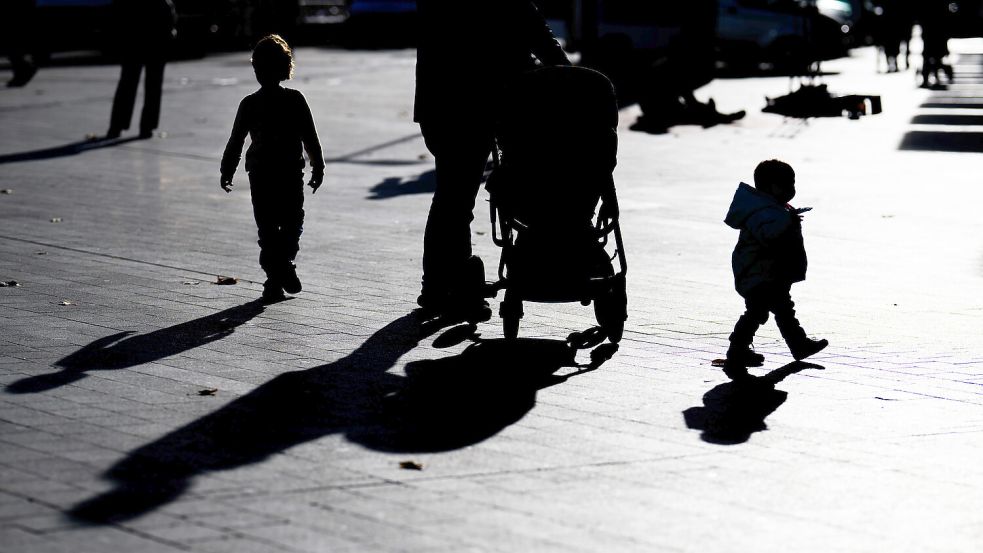 Zwei Kinder und ein Mann mit Kinderwagen laufen über einen Platz. Die Bevölkerung in Ostfriesland schrumpft – genau wie im ganzen Land. Foto: Julian Stratenschulte/dpa