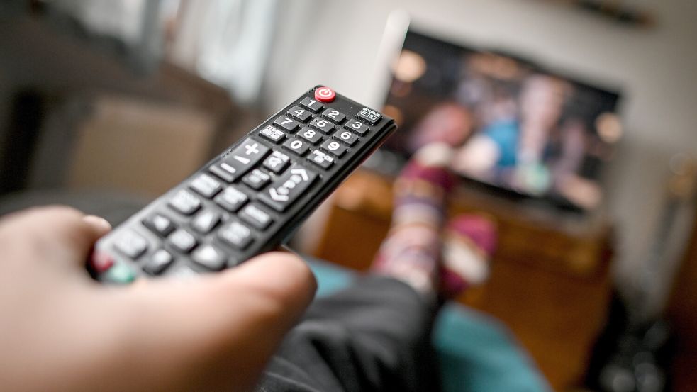 Ein Mann sitzt mit einer Fernbedienung vor dem Fernseher. In Pewsum haben Anwohner der Helenenstraße seit Wochen keinen Fernsehempfang mehr. Symbolfoto: Britta Pedersen/dpa
