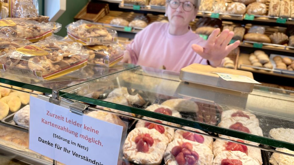 Mit Hinweisschildern kommuniziert das Team der Bäckerei Hinrichs, hier Astrid Baetke, sein aktuelles Internetproblem ganz offen. Foto: Susanne Ullrich
