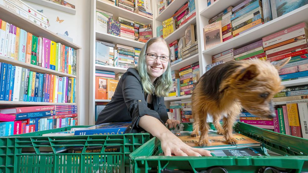 Diana Rösemann hockt mitten in ihrem Bücherraum in Remels. Hündin Luna steht auf einem der Bücherkisten. Foto: Klaus Ortgies