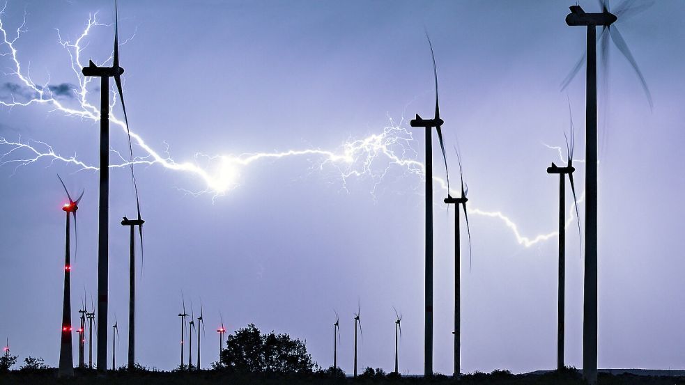Ein mächtiger, verzweigter Gewitterblitz leuchtet über der nächtlichen Landschaft mit einem Windpark. Foto: Patrick Pleul/DPA